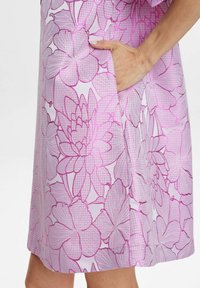 Rochie cu mânecă scurtă, decorată cu un model floral roz cu contururi violete. Include un buzunar lateral și are o textură netedă.