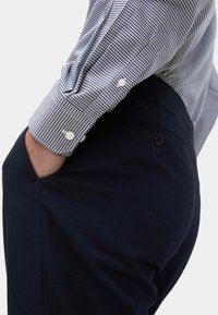 Camicia a scacchi bianca e nera con polsini a bottoni, abbinata a pantaloni blu navy con tasca laterale e dettaglio a bottoni.