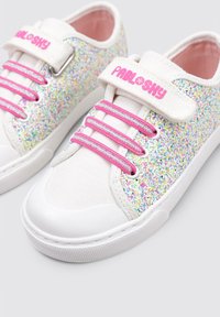 Zapatillas blancas brillantes con cordones rosas y una correa de Velcro, que presentan una suela de goma blanca brillante y acentos de purpurina texturizados y multicolores.