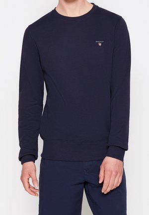 Sudadera azul marino hecha de una tela suave, con cuello redondo, mangas largas, puños acanalados y un pequeño logo en el pecho.