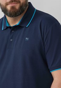 Granatowa koszulka polo z kontrastującymi akcentami w kolorze turkusowym na kołnierzu i rękawach, z trzema guzikami przy plisce oraz małym logo na piersi.