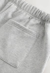 Light gray sweatpants fabric with elastic waistband and a large rectangular back pocket stitched on the right side.
