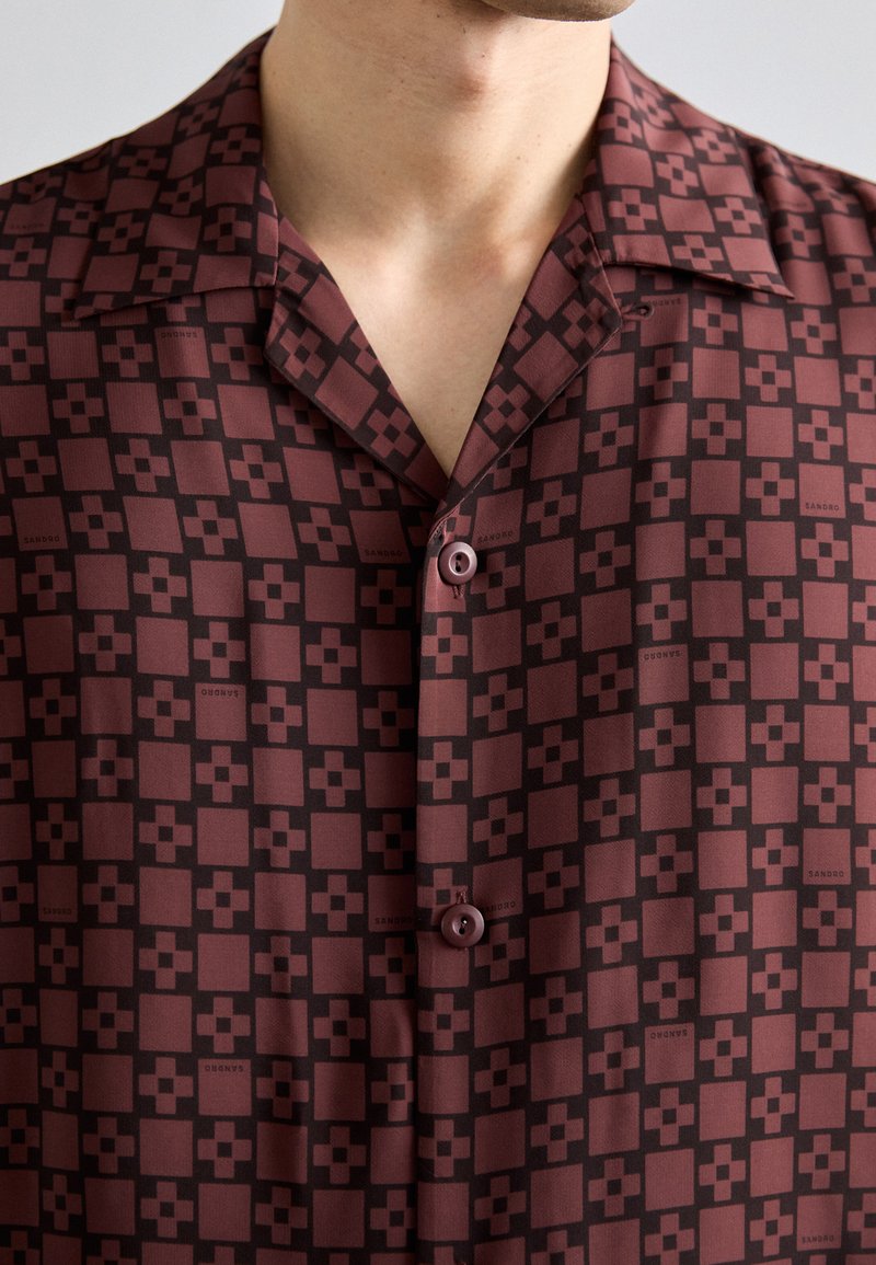 Camicia a maniche corte con un motivo geometrico borgogna e nero, realizzata in tessuto morbido, con colletto a profilo e chiusura a bottoni.