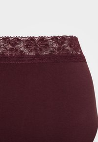 Μπορντό εσώρουχα με ψηλή μέση και λουλουδάτη δαντέλα στην κορυφή, διαθέτοντας μαλακό και ελαστικό ύφασμα για άνεση και καλή εφαρμογή.