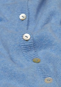 Lichtblauwe gebreide trui met vijf parelknopen aan de voorkant, met een zachte textuur en een subtiel ribbelpatroon.