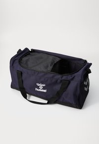 Mørkeblå Hummel sport duffelbag med sorte håndtak og nettinglomme på siden, delvis åpnet som viser svart innredning.