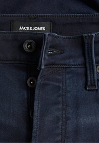 Vaqueros de mezclilla azul oscuro con una textura suave, que presentan una cremallera, dos botones negros y una etiqueta que dice "JACK & JONES."