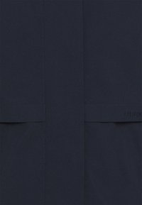 Marineblaue Regenjacke mit glatter Textur, gerader Passform und zwei frontalen Taschen. Mit einem dezenten Markenlogo am Saum.