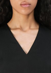 Zwart v-hals top met een gladde textuur, een diepe halslijn en een minimalistisch ontwerp, gericht op strakke lijnen en ingetogen elegantie.