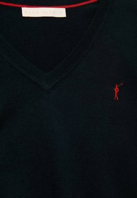 Pull en V bleu marine foncé en tissu tricoté ; présente un accent rouge le long de l'encolure et un petit logo rouge brodé près de la poitrine.