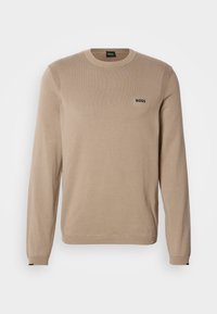 Beżowy sweter dziany z długimi rękawami, okrągłym dekoltem, prążkowanymi detalami i małym czarnym logo 'BOSS' na piersi. Miękka faktura, klasyczny krój.