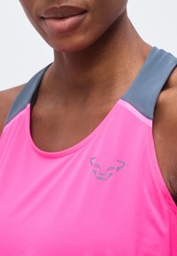 Κοντινό πλάνο ενός ατόμου που φοράει ροζ αθλητικό τοπ με γκρίζες τιράντες και μικρό γκρίζο λογότυπο πάνθηρα στο στήθος.