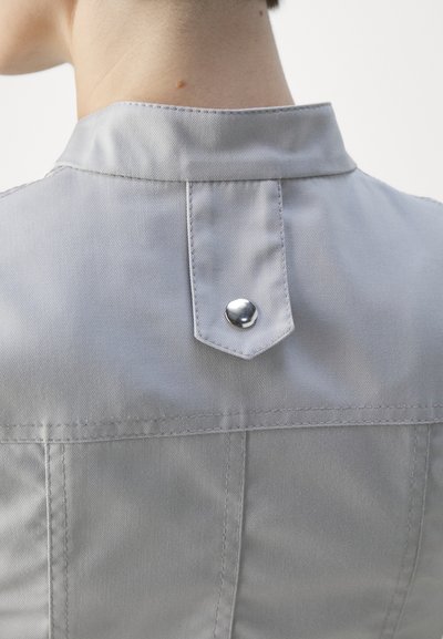 Light gray fitted jacket collar with a pointed back and single metallic snap closure. Smooth fabric with visible seam lines and subtle texture.
