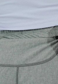 Pantalones cortos de cuadros verdes, ligeros y con un aspecto texturizado. Cuentan con una cinturilla elástica y un bolsillo lateral con cierre de cremallera negra.