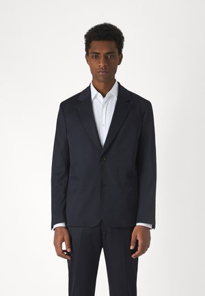 Navy tailored suit jacket with notch lapels, single button closure, and side pockets. Complemented by a crisp white dress shirt.