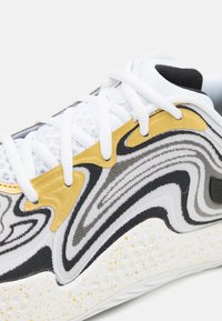 Schoen met een gestructureerde bovenkant met witte, zwarte en gouden golfpatronen. Rubberen zool met een gespikkelde witte afwerking en witte veters.