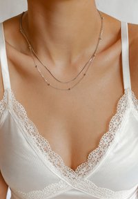 Collane sovrapposte in argento con catene lisce e curve e piccoli perle rotonde, indossate con un top di pizzo crema.