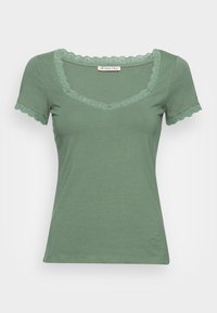 Maglietta verde a maniche corte con scollatura in pizzo ondulato e bordi delle maniche. Realizzata in un tessuto morbido, presenta una silhouette aderente.