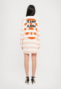Vestito a righe in rosa pastello e bianco con la scritta grafica nera e arancione "JEANS" sulla schiena; presenta maniche lunghe e una vestibilità comoda.