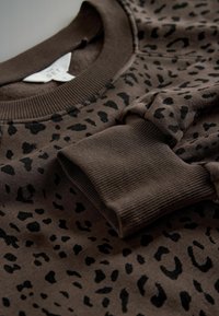 Hnedý sveter s čiernym leopardím vzorom, s rebrovaným golierom a manžetami, mäkkou textúrou a pohodlným dizajnom.