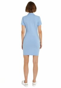 Abito polo blu chiaro, maniche corte, forma aderente, realizzato in tessuto liscio, con colletto. Abbinato a sneaker bianche.