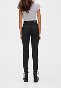 Zwarte high-waisted jeans met een aansluitende pasvorm, vergezeld van een gestreepte top met korte mouwen. Beschikt over twee achterzakken en een blauwe merklabel.