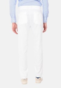 Pantaloni di lino bianchi con un design a gamba dritta, dotati di tasche posteriori e abbinati a sneakers in suede grigio chiaro. Visti da dietro.