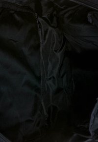 Interno di una borsa in nylon nero con un tessuto liscio e riflettente, dotata di tasche laterali e chiusura con zip. Design minimalista senza motivi visibili.