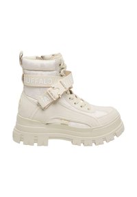 Bota beige hasta el tobillo con un diseño acolchado, suela gruesa, parte delantera con cordones y una correa lateral con la palabra "BUFFALO" en blanco. Textura mate.