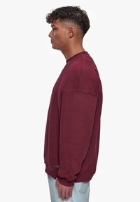 Bordeauxfarbene Rundhals-Sweatshirt mit lockerer Passform, strukturierter Stoff und gerippten Bündchen und Saum. Dezentes Branding am Saum.