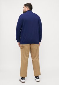 Sudadera navy con cuello alto, tejido suave, mangas largas, combinada con pantalones cargo khaki que cuentan con bolsillos laterales y un corte holgado.