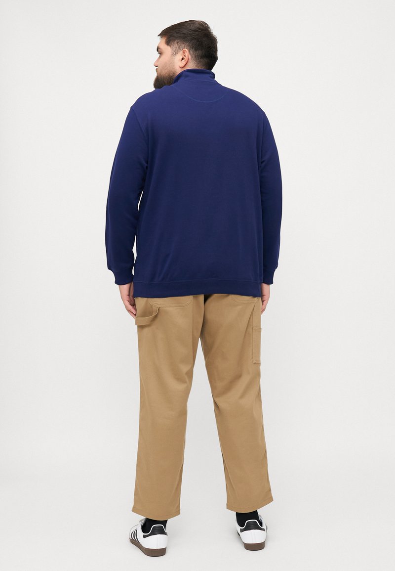 Marine pullover met hoge kraag, zachte stof, lange mouwen, gecombineerd met kaki cargobroek met zijzakken en een ontspannen pasvorm.