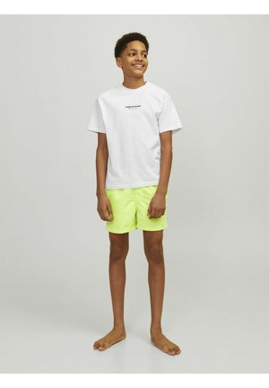Camiseta blanca de algodón con texto negro, combinada con pantalones cortos neón verdes brillantes, que presenta un corte clásico y una textura suave.