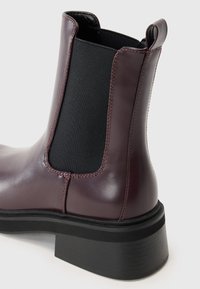 Botín Chelsea de cuero burdeos con paneles laterales elásticos, tacón texturizado y suela de goma negra, con un acabado suave y acentos cosidos.