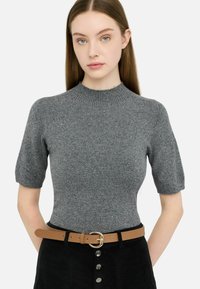Top grigio a maniche corte in maglia con collo alto e dettagli di luccichio sottili, abbinato a una cintura color tan con fibbia circolare su una gonna nera.