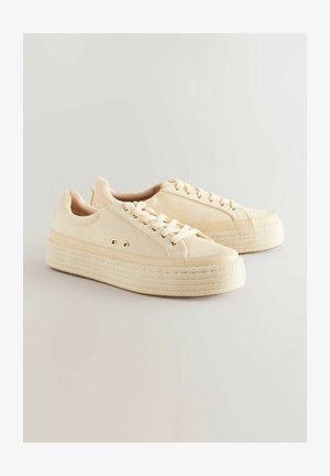 Beige vászon sportcipők texturált felsőrésszel, kerek orral és juta talppal, amely fonott mintázattal és aranyszínű fémlyukakkal rendelkezik.