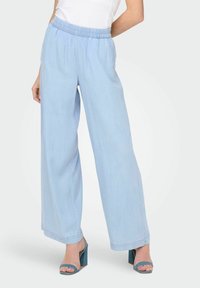 Pantalons larges bleu clair en tissu doux, avec une taille élastique. Associés à des sandales à talons hauts teal.