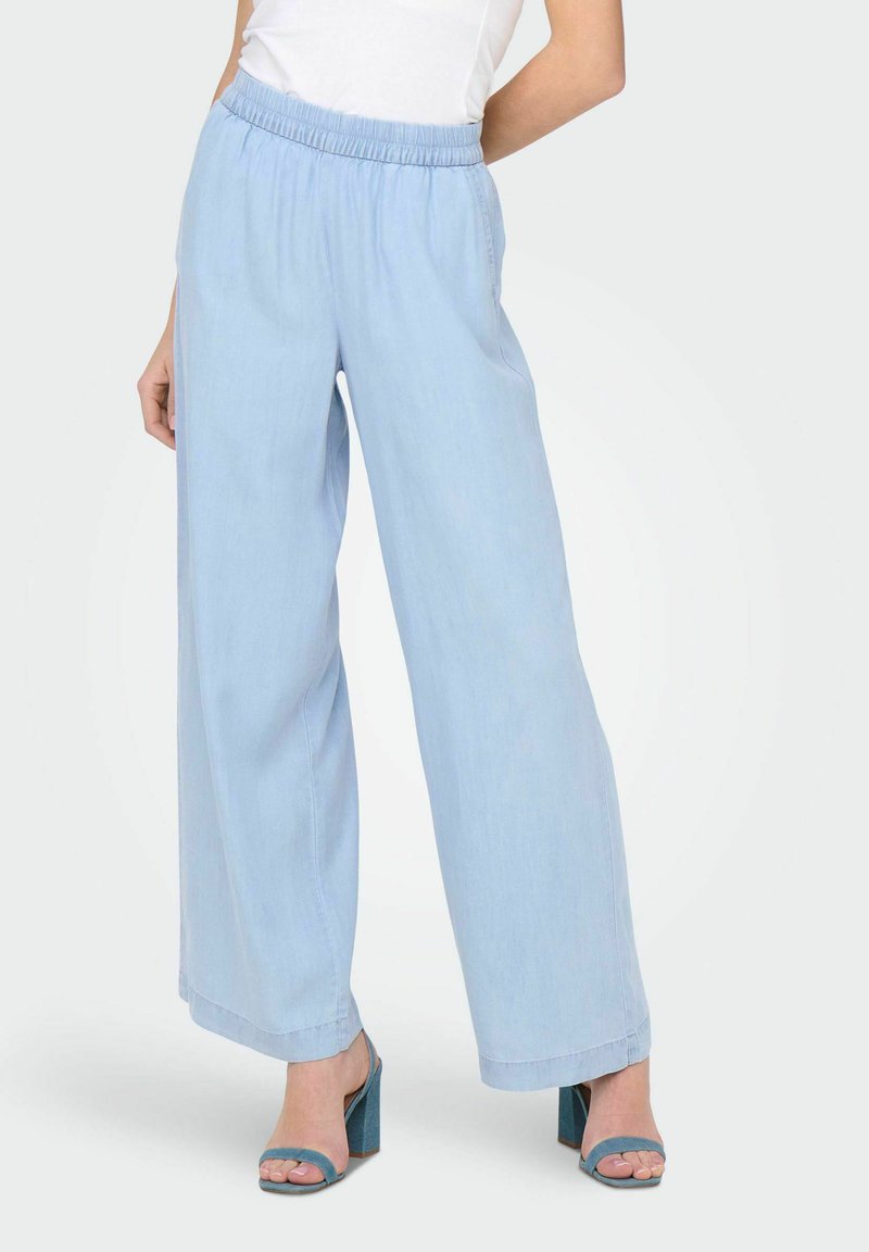 Pantalons larges bleu clair en tissu doux, avec une taille élastique. Associés à des sandales à talons hauts teal.