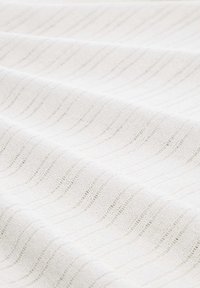 Bílá tkanina s texturovaným vzorem vlny; měkký pletený materiál s jemným leskem a různou tloušťkou příze.