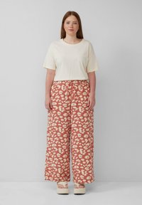 Losse crème t-shirt gecombineerd met brede, rustkleurige broek met een licht luipaardpatroon. Het model draagt platform schoenen.