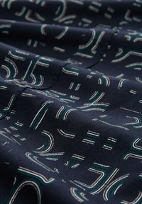 Navy stof met abstracte lijnpatronen in wit en teal, met een gladde textuur en een lichte glans, gevouwen met subtiele plooien.