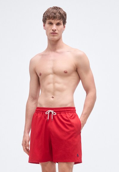 Calções de banho vermelhos com cintura elástica e cordão branco, apresentando um pequeno logótipo no lado inferior esquerdo. Textura de tecido lisa.