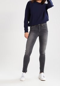Sudadera de color navy combinada con jeans skinny grises; los jeans presentan detalles desgastados y dobladillos desflecados, complementados con zapatillas blancas.