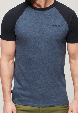 Tummansininen lyhythihainen t-paita, jossa on raglan-mustat hihat. Kevyt kangas, pyöreä pääntie, hillitty logo rinnassa, vartalonmyötäinen malli.