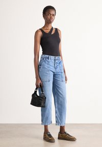 Top de tirantes negro acanalado, jeans de mezclilla azul claro de cintura alta con bolsillos, bolso de piel sintética negro y zapatillas con estampado y acentos amarillos.