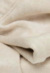 Beige gebreide stof met een zachte textuur, met een fijne, gelijkmatige weving en subtiele stiksels. Vloeiend met een lichte glans.