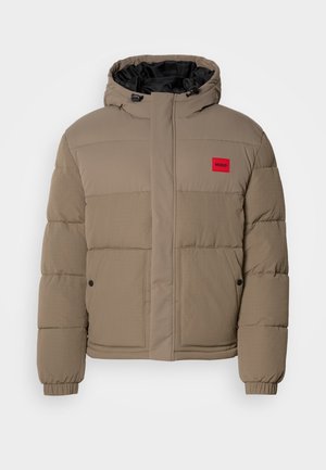 Steppjacke in hellbraun, mit verstellbare Kapuze, Frontreißverschluss und einem roten Logo-Patch auf der Brust. Ausgestattet mit elastischen Bündchen und Taschen.