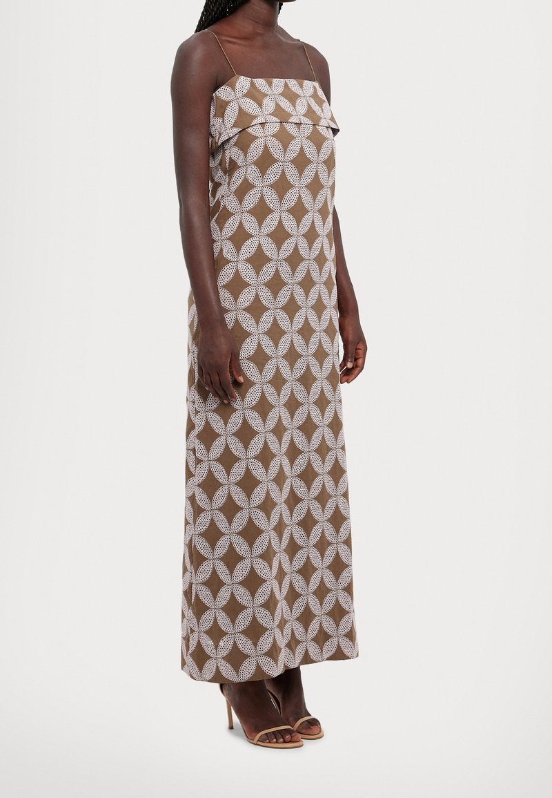 Brown maxi dress with white geometric pattern, strapless design, textured ruffle at the top, and a straight silhouette. Heels visible below.
