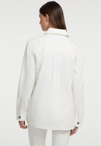 Witte, zware katoenen jas met een klassieke kraag, knoopmanchetten en een rugplooi voor een relaxte pasvorm. Soepele textuur zonder zichtbare patronen.