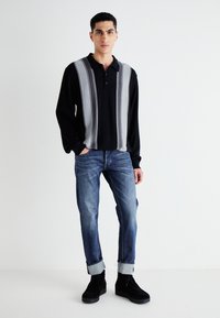 Camisa polo de manga larga negra con rayas verticales grises, combinada con jeans azules ajustados y zapatos de plataforma negros. Diseño simple y moderno.